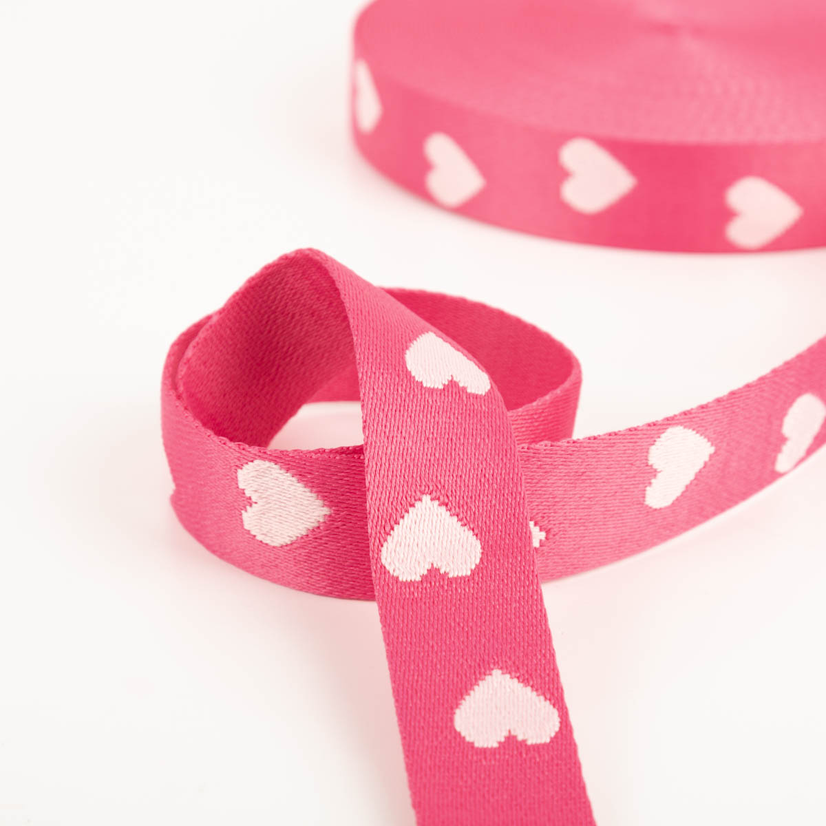 Gurtband Herzen pink rosa Breite: 4cm Detailaufnahme eines pinken Gurtbands mit rosa Herzmotiv, Band liegt locker geschwungen auf weißem Untergrund