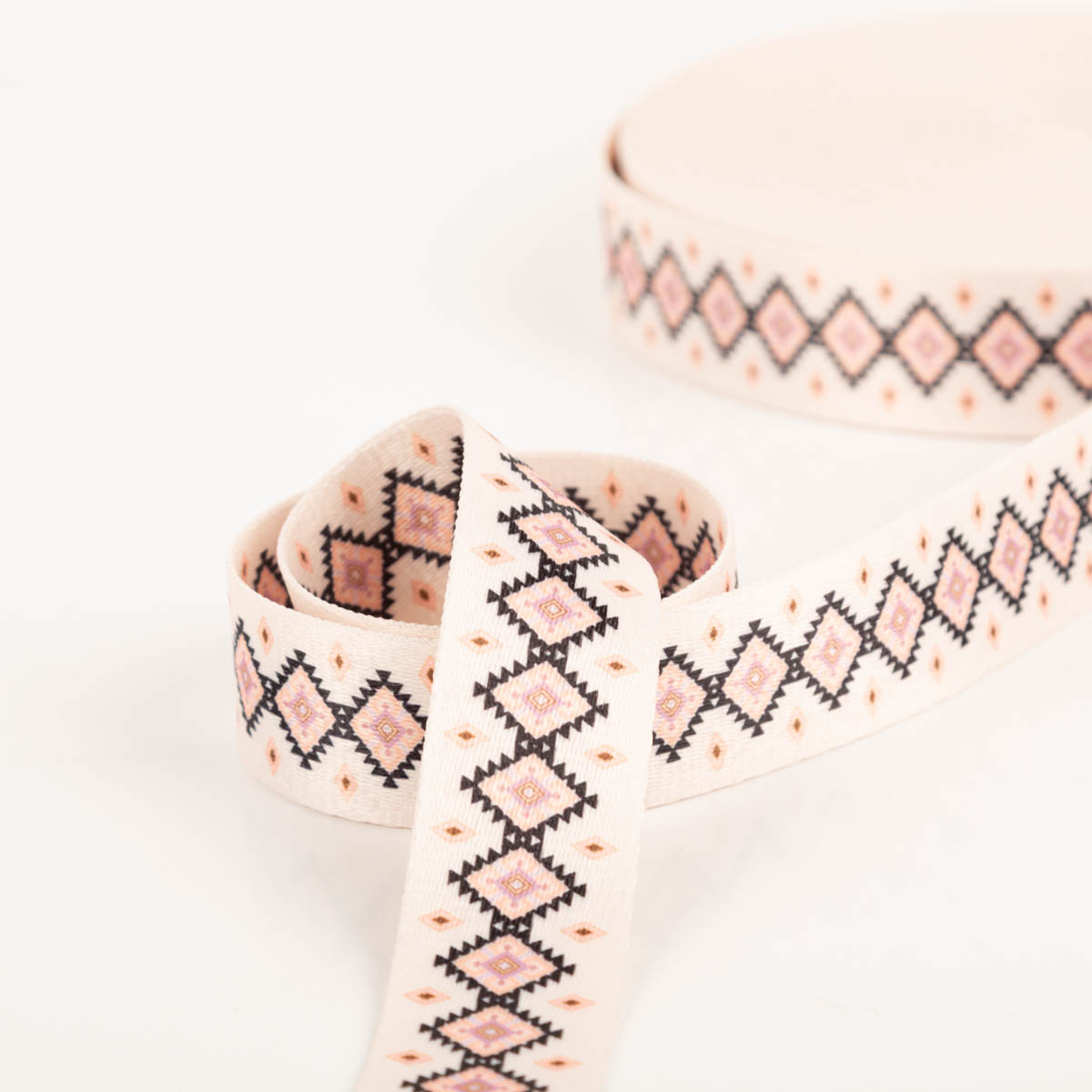 Gurtband Rauten creme rosa schwarz Breite: 4cm cremefarbenes Gurtband mit rosa und schwarzen Rauten zur Spirale gelegt, Nahaufnahme
