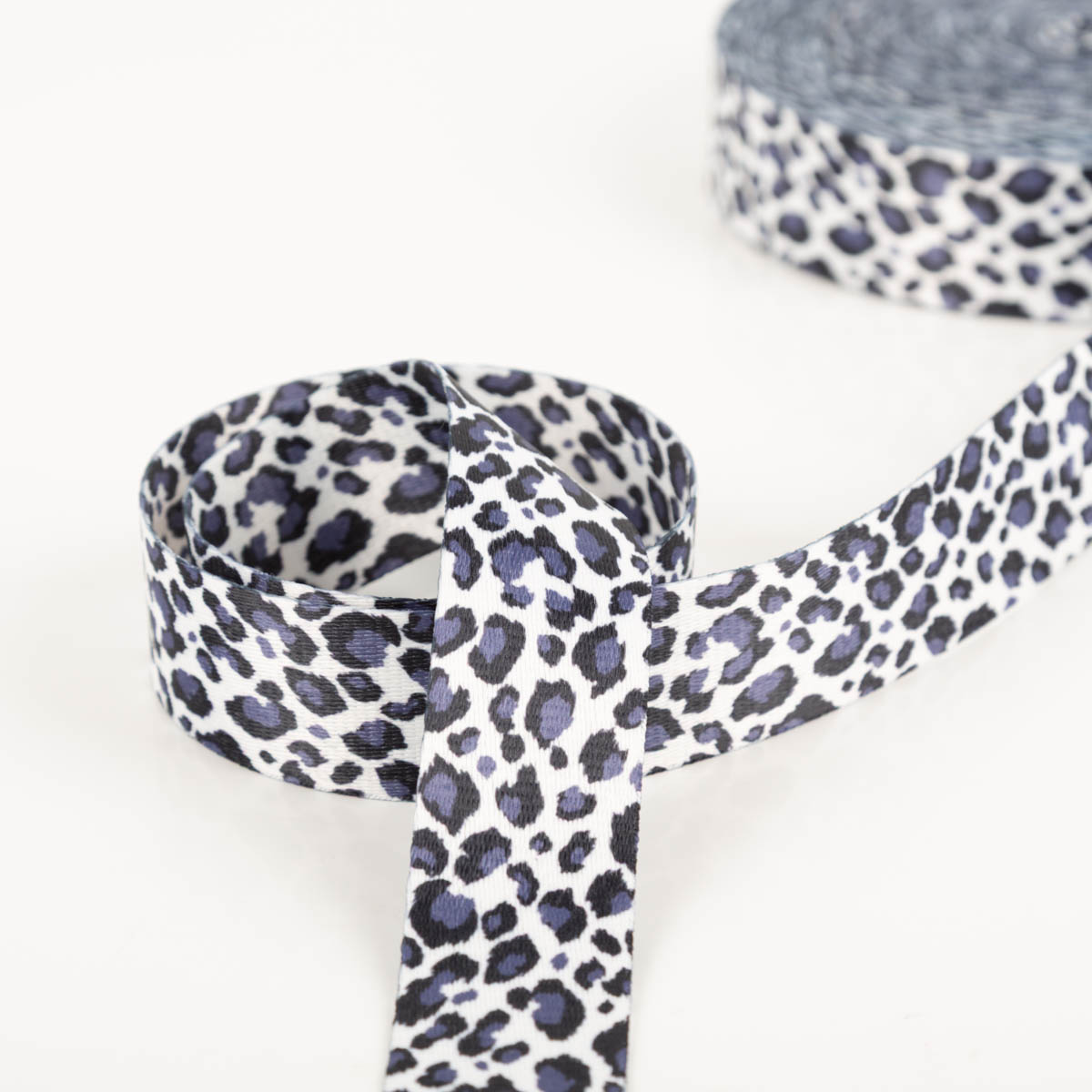 Gurtband Leopard weiß dunkelblau Breite: 4cm breites Gurtband in Weiß mit dunkelblauem Leomuster, im Vordergrund locker als Schlaufe gelegt