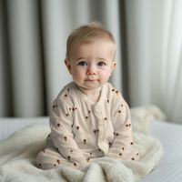 Baby in einem Langarmshirt aus naturfarbenem Rippjersey mit kleinen Pilzen auf einer weichen Decke