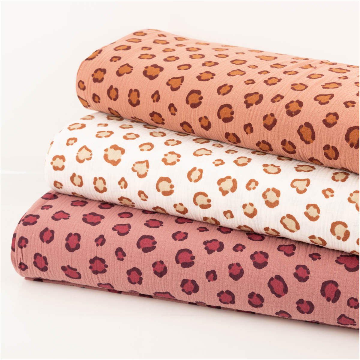 drei Musselin-Stoffe mit Leomuster und Herzen in verschiedenen Farben als Stoffstapel