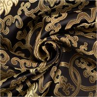 schwarzer Brokatstoff mit goldfarbenen Ornamenten, zur Spirale gedreht, Muster und Glanz im Detail sichtbar