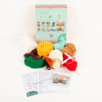 Häkelset Pommes Hähnchenkeule und Milchshake DIY Set mehrfarbige Wollknäuel, Häkelanleitung und Zubehör vor hellblauer Verpackung mit gehäkelten Snackfiguren