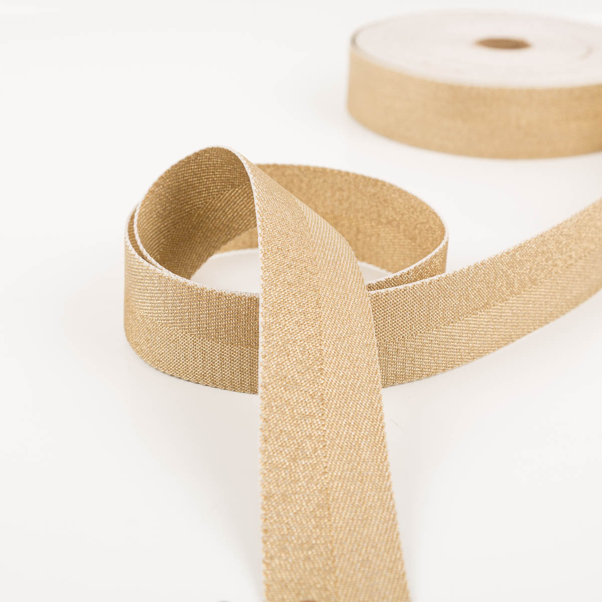 96578-Gurtband-metallic-Lurex-gold-4cm-Breite-IMG-0325.jpg Gurtband metallic Lurex gold 4cm zur Schlaufe gelegt vor der Rolle, schimmernde Oberfläche