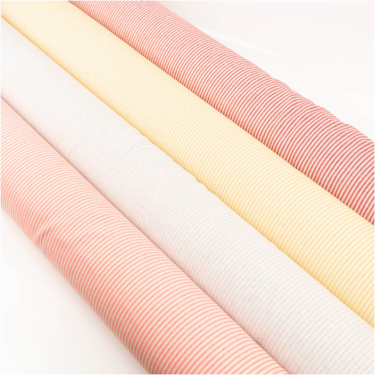 Dekostoff Dobby Streifen 3mm gelb beige 1,40m Breite gestreifte Stoffrollen in Gelb und Beige sowie Rosa-Tönen, nebeneinander auf hellem Untergrund angeordnet