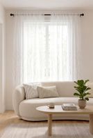 Weißer Voile-Vorhang mit Gräsern am Fenster eines hellen Wohnzimmers Weißer Voile-Vorhang mit Gräsern am Fenster eines hellen Wohnzimmers